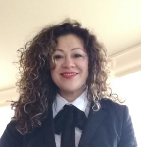 Silvia, a curly-haired woman wearing a suit, smiles for a professional photo.